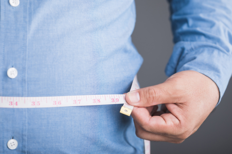 An adult wearing a tight shirt using a measuring tape around their waist