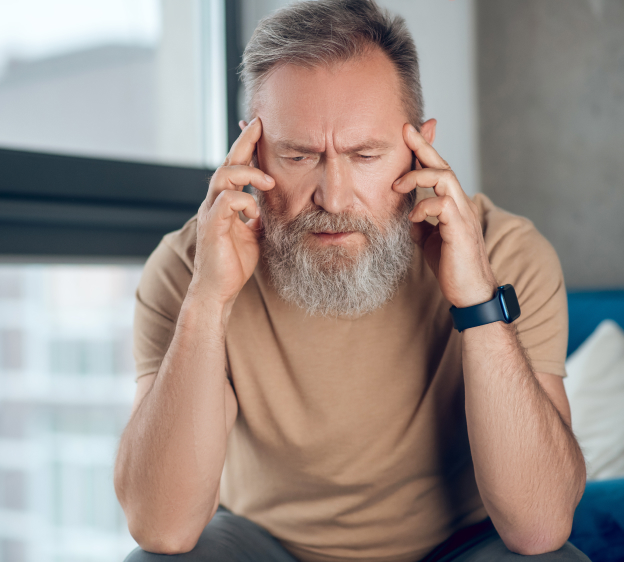 An older adult bearded man suffering from a headache and holding his temples with his fingers