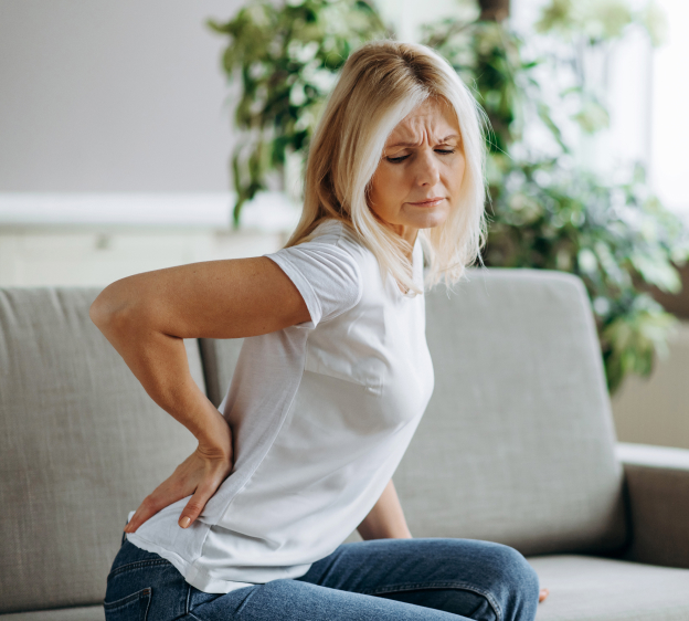 Blonde adult woman looking upset while holding her lower back with her right hand