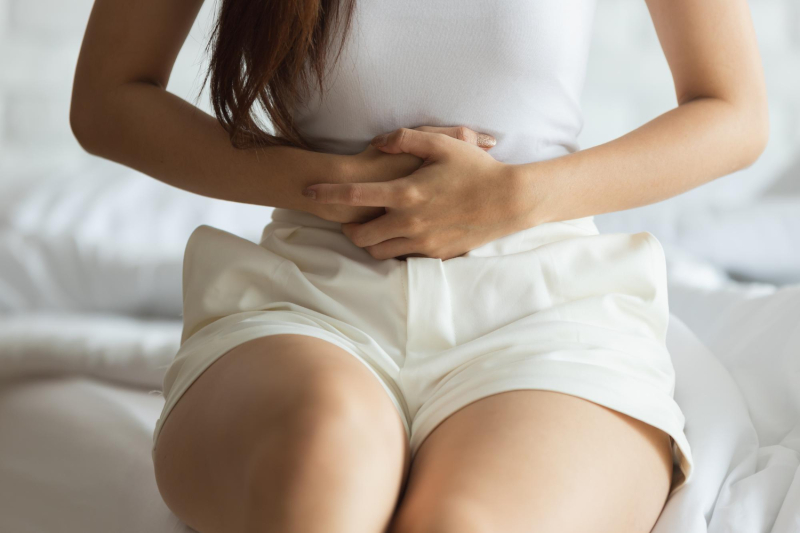 Unidentified woman sitting on a bed holding her stomach