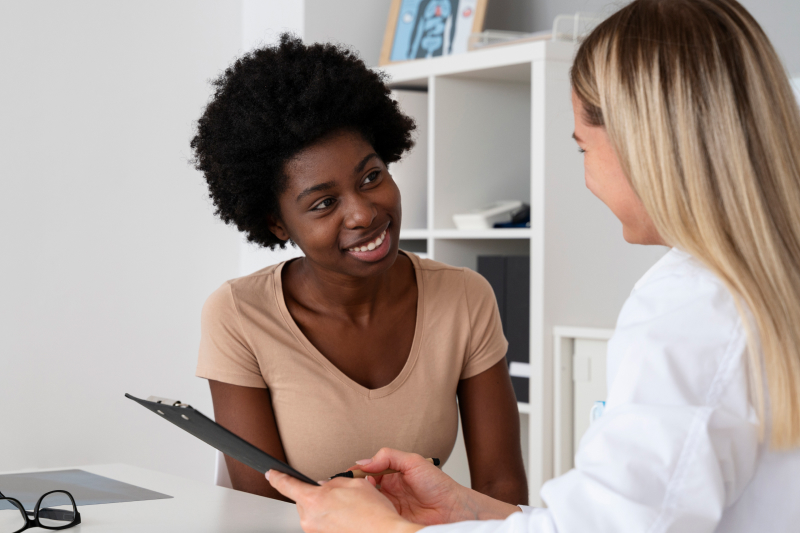 Black woman smiles and looks at medical provider who is holding a clipboard