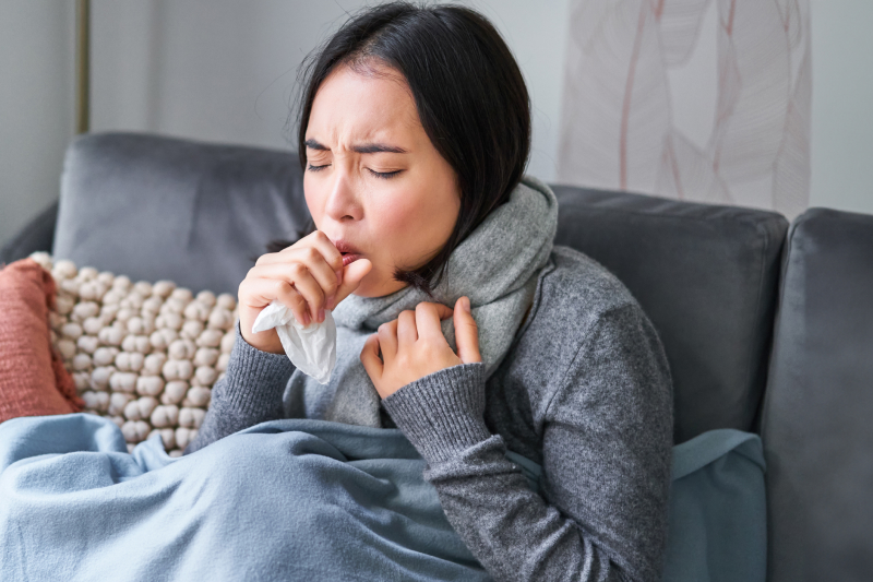 Woman coughing feeling sick sitting under blanket with scarf 