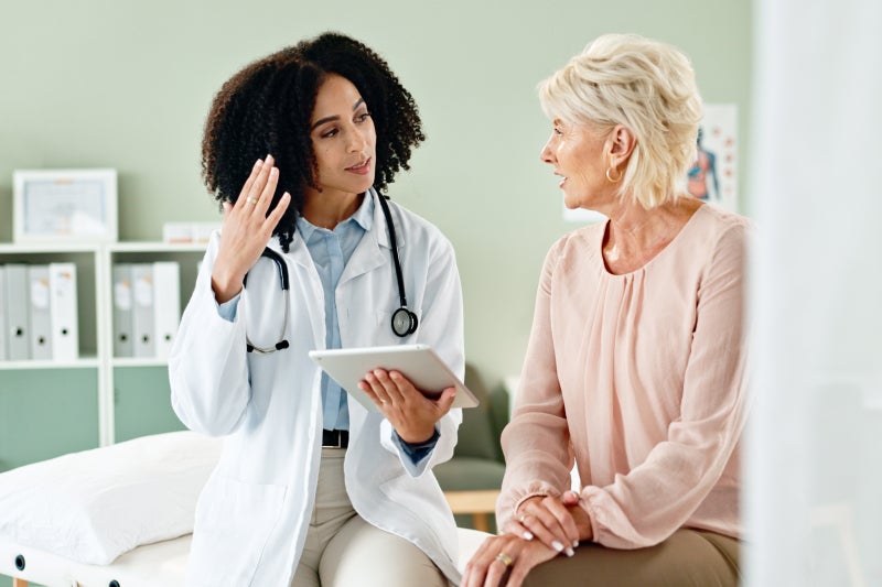 Woman doctor and consulting with patient in an examination room and sharing a tablet