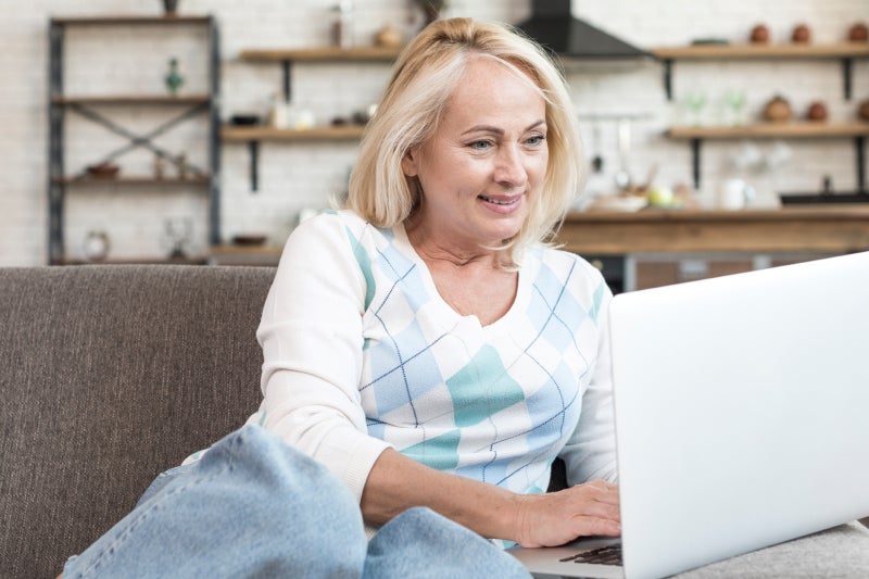 Blond adult woman smiling while looking at and using a laptop