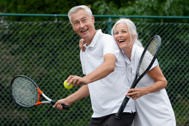 Two older adults playing tennis and smiling