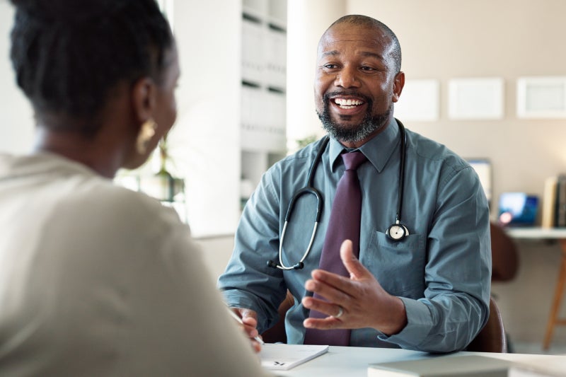 Black medical provider sitting and speaking with a patient in an office