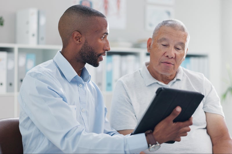 A professional shares information on a tablet with an older man in a bright office
