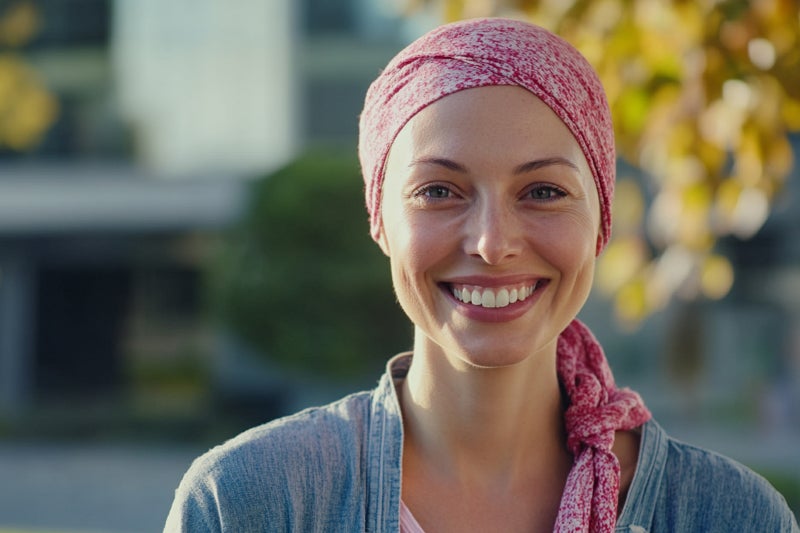 A cheerful woman with a pink headscarf smiles warmly at the camera