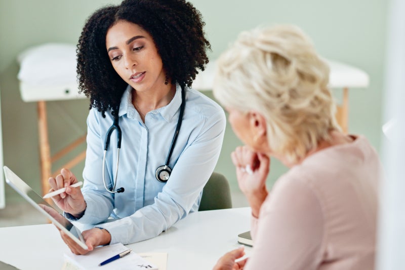 Female doctor explains medical information on a tablet to an older woman during a calm, supportive consultation in a bright clinic.
