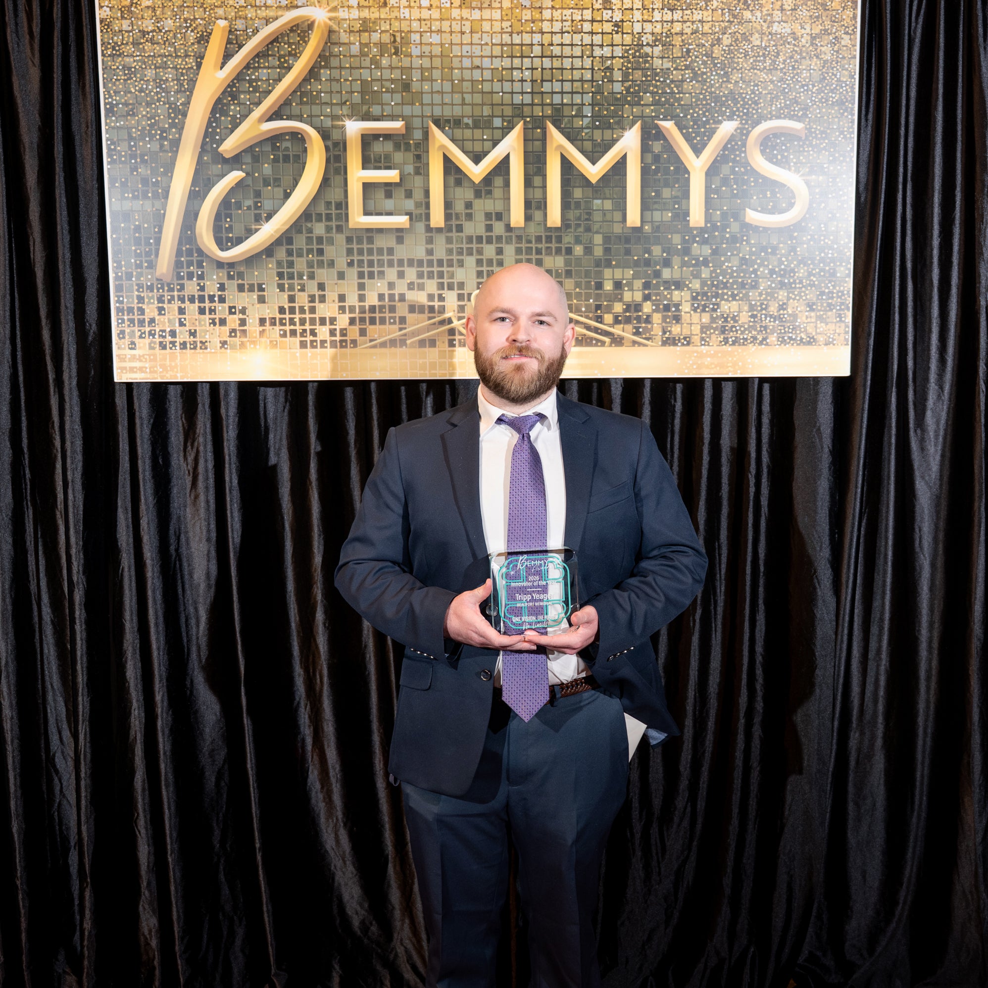 Bruce "Tripp" Yeager holds a 2026 Bemmy Award in front of a black backdrop and hanging sign that reads BEMMYS.