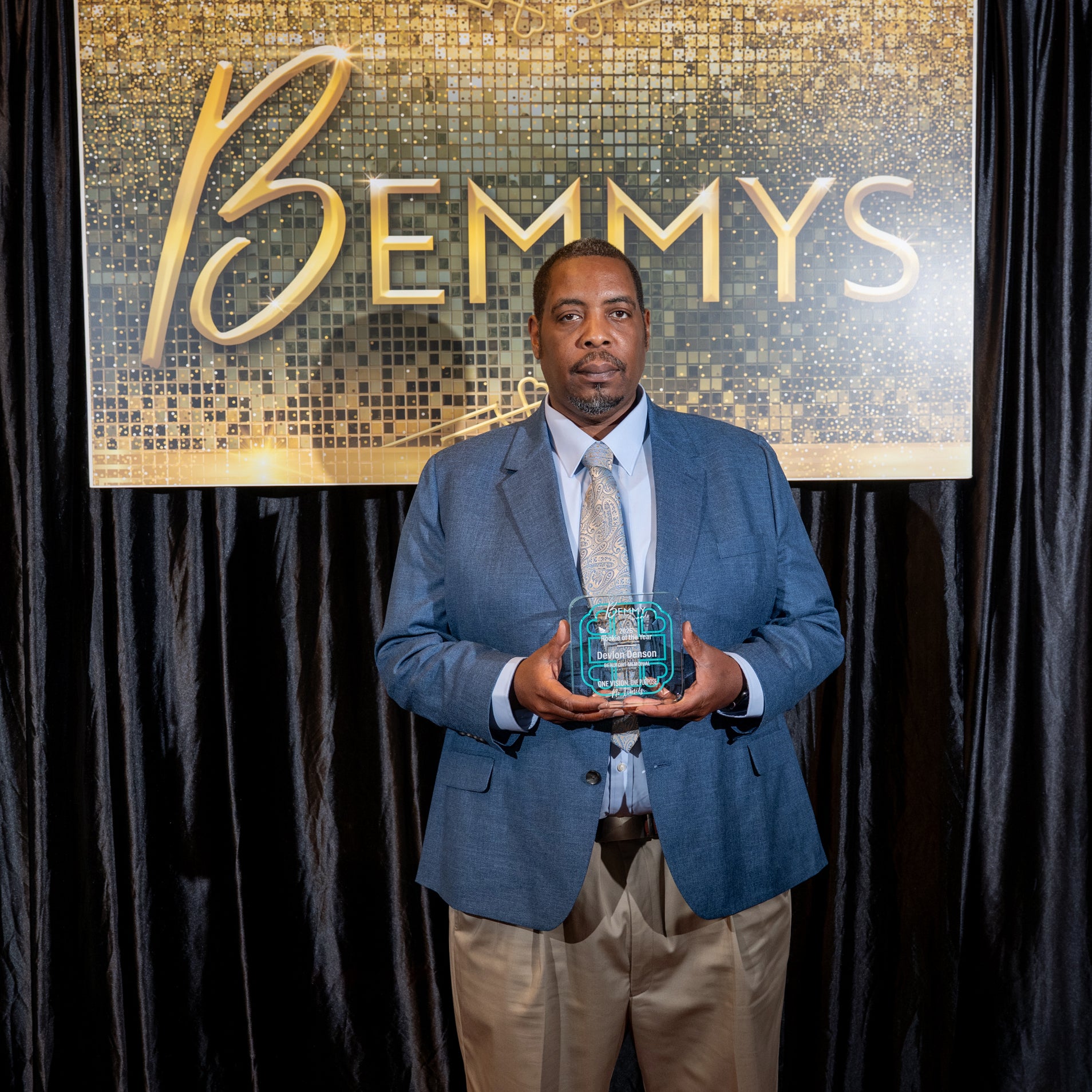 Delvon Denson holds a 2026 Bemmy Award in front of a black backdrop and hanging sign that reads BEMMYS.