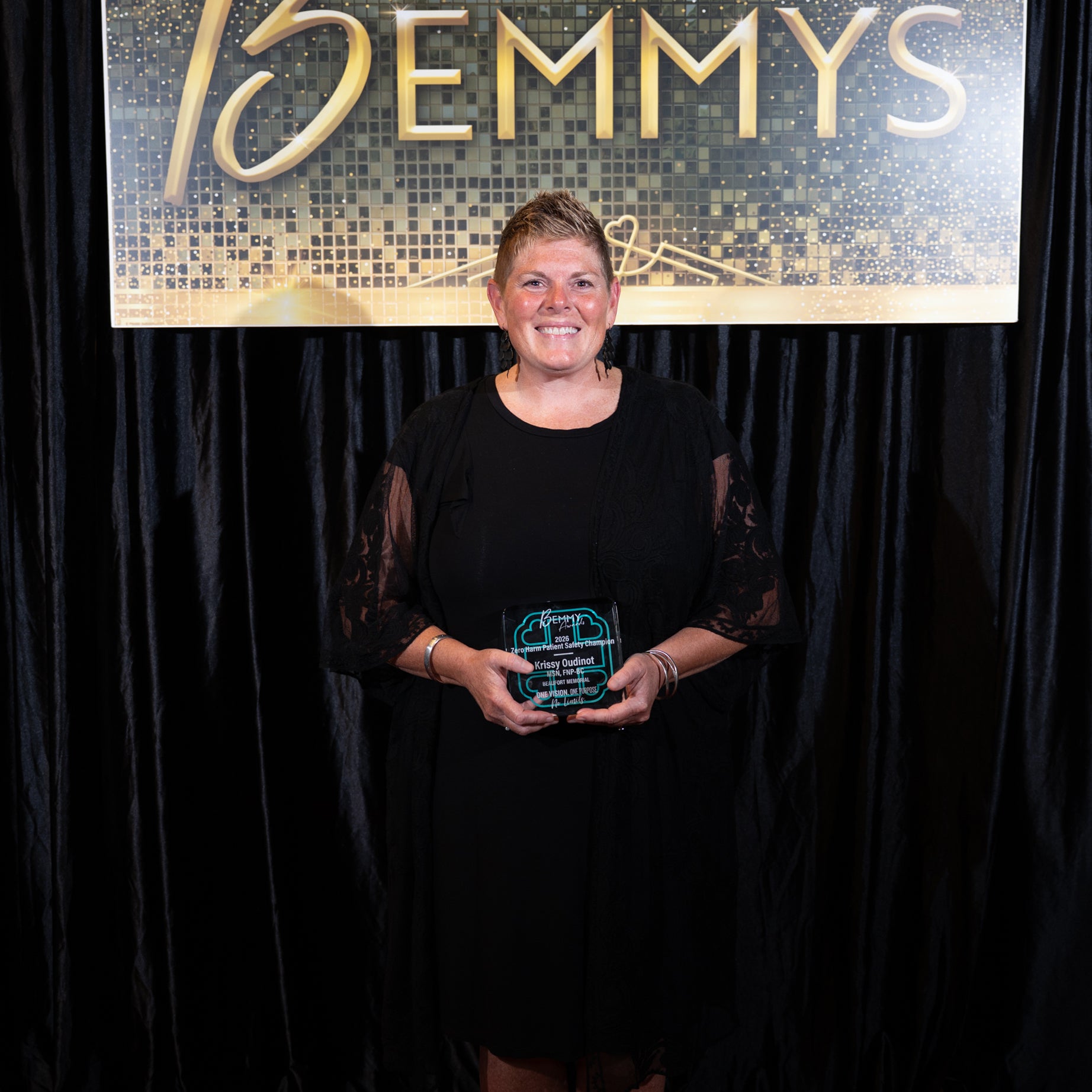 Krissy Oudinot holds a 2026 Bemmy Award in front of a black backdrop and hanging sign that reads BEMMYS.