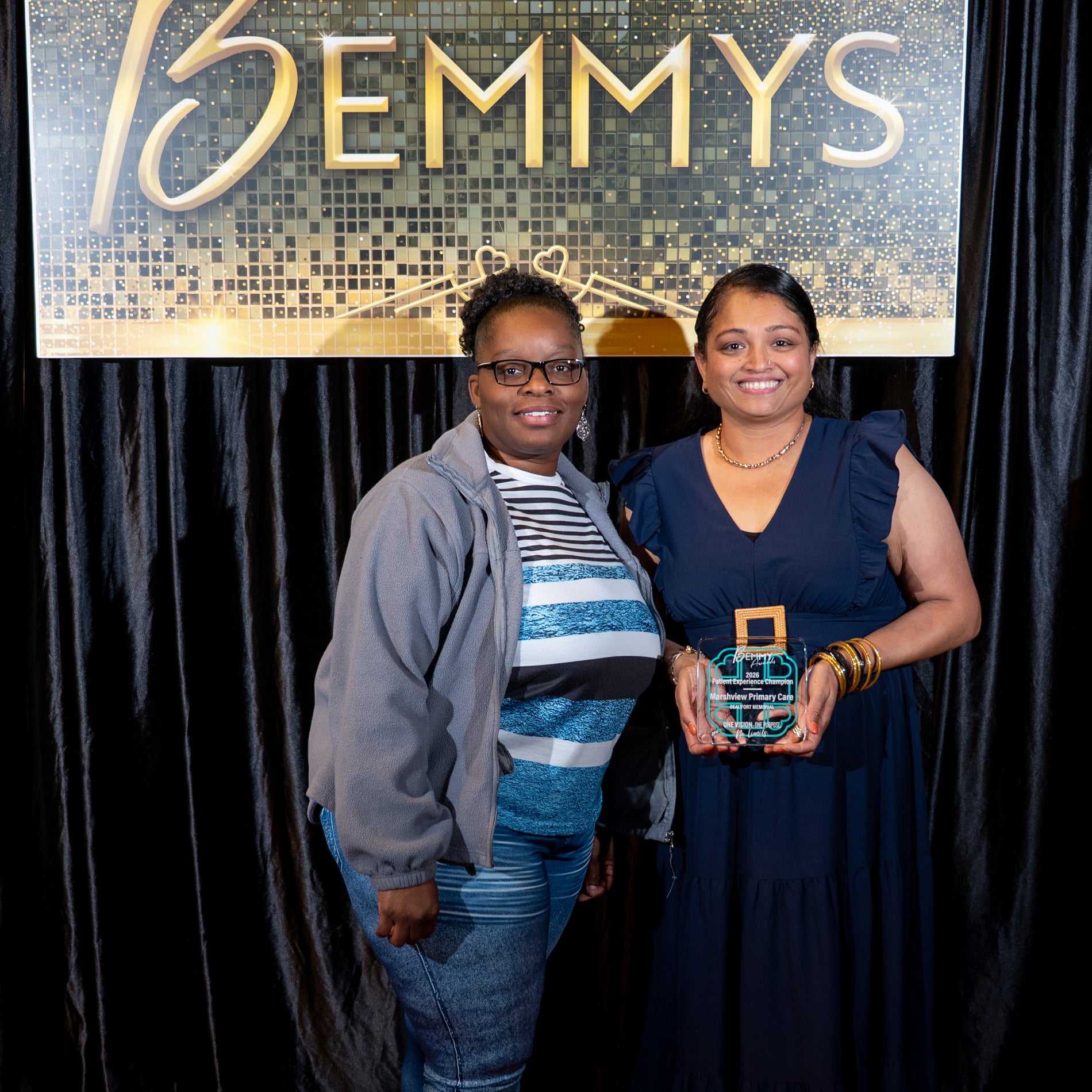 Two staff members from Beaufort Memorial Marshview Primary Care pose for a photo in front of a black backdrop, one of them holding a 2026 Bemmy Award.