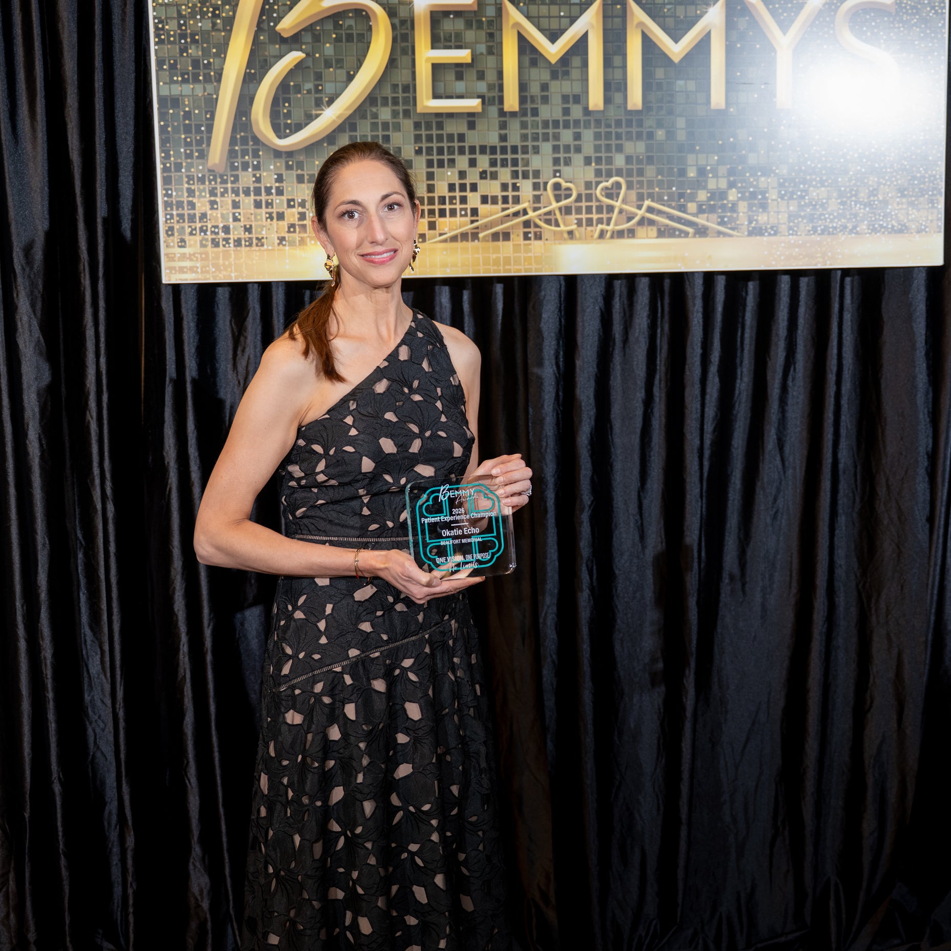 A staff member from the Okatie Echo Department holds a Bemmy award posing in front of a black backdrop.