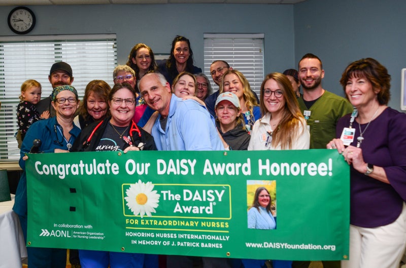 Beaufort Memorial employees join ICU nurse Candy Chappell and her family for a photo behind a DAISY Award recognition banner