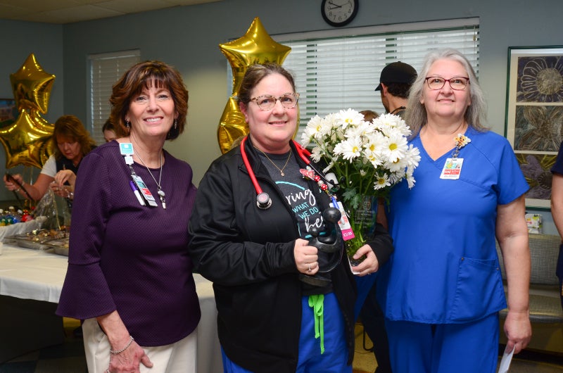 Candy Chappell, holding a vase of white daisies, stands between Colleen Duerr and Deborah Murray for a photo.