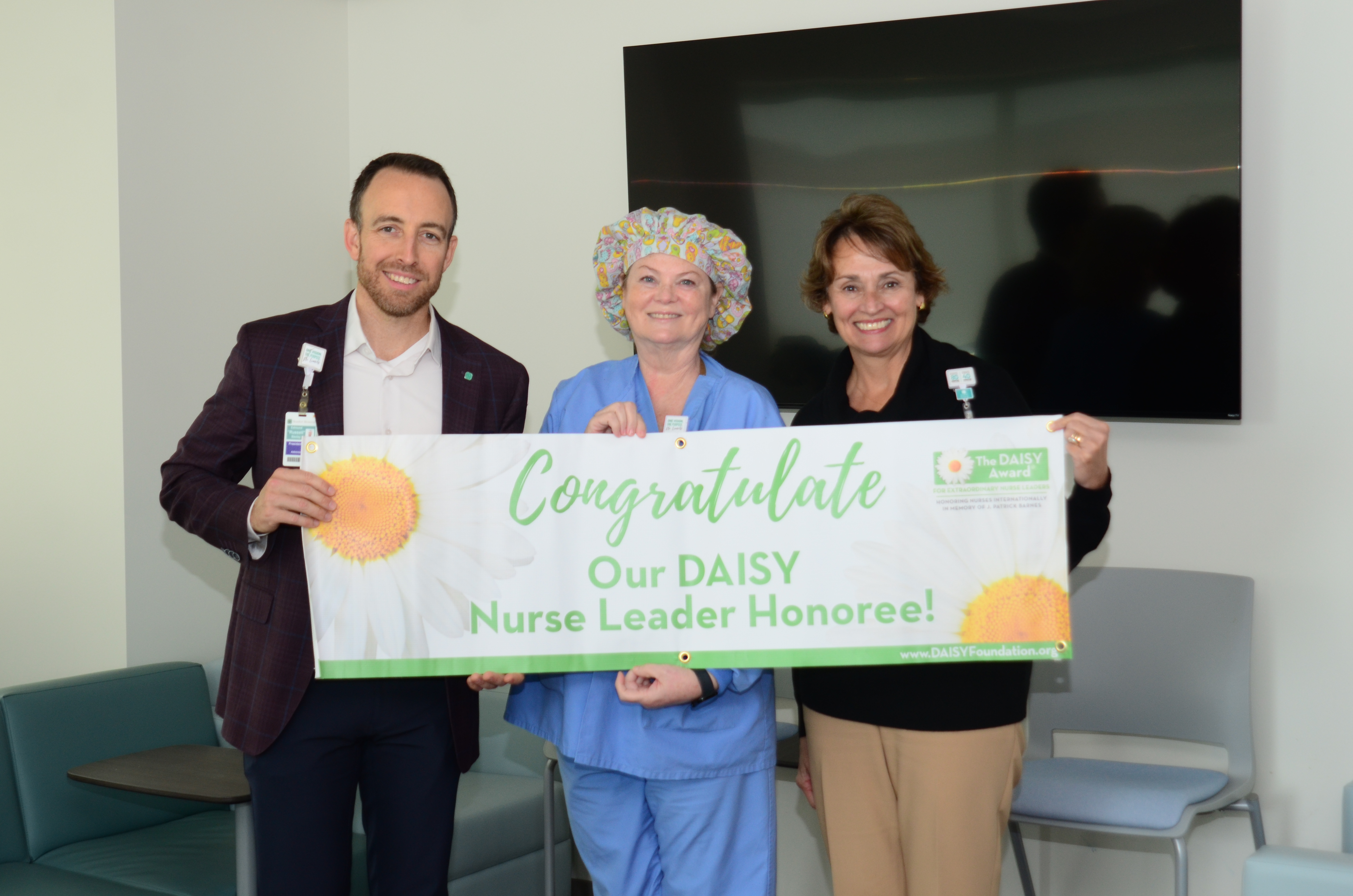 Russell Baxley, Denise Lindsey and Karen Carroll hold a banner congratulating Denise for her DAISY Nurse Leader award