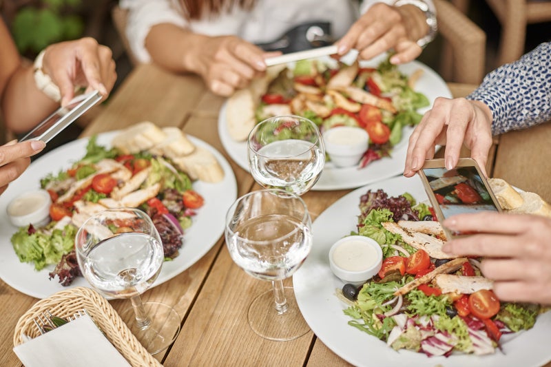 Nearly overhead view of three full plates of healthy food on a table with hands next to them