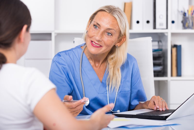 Female doctor listening to female patient in a clinical office setting.