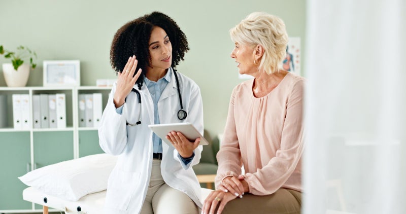A female care provider speaks with a female patient in an exam room of a medical clinic