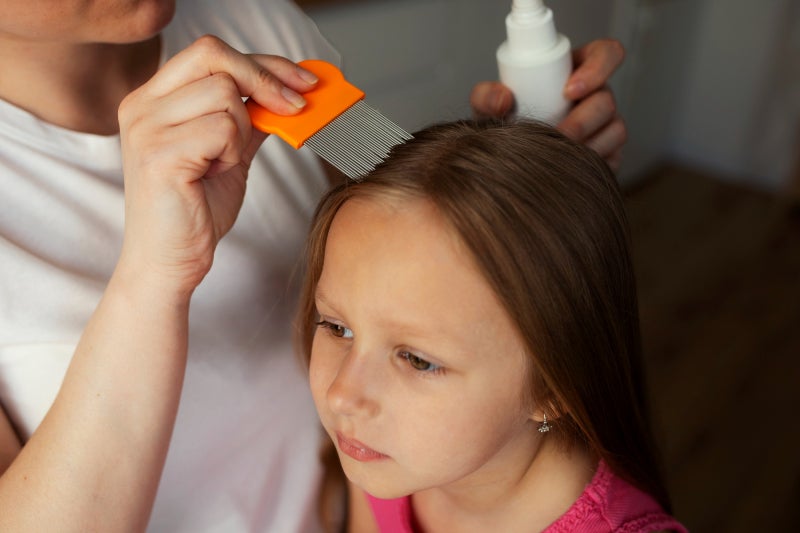 Younger girl getting her head and hair checked for lice from an adult using a lice comb.
