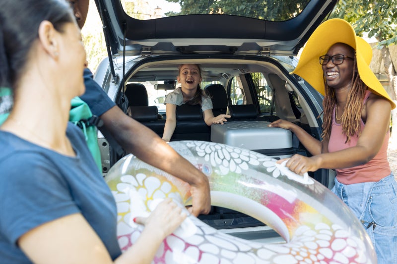 Multiethnic family or friends loading luggage and water toys into the back of a car for a warm weather trip.