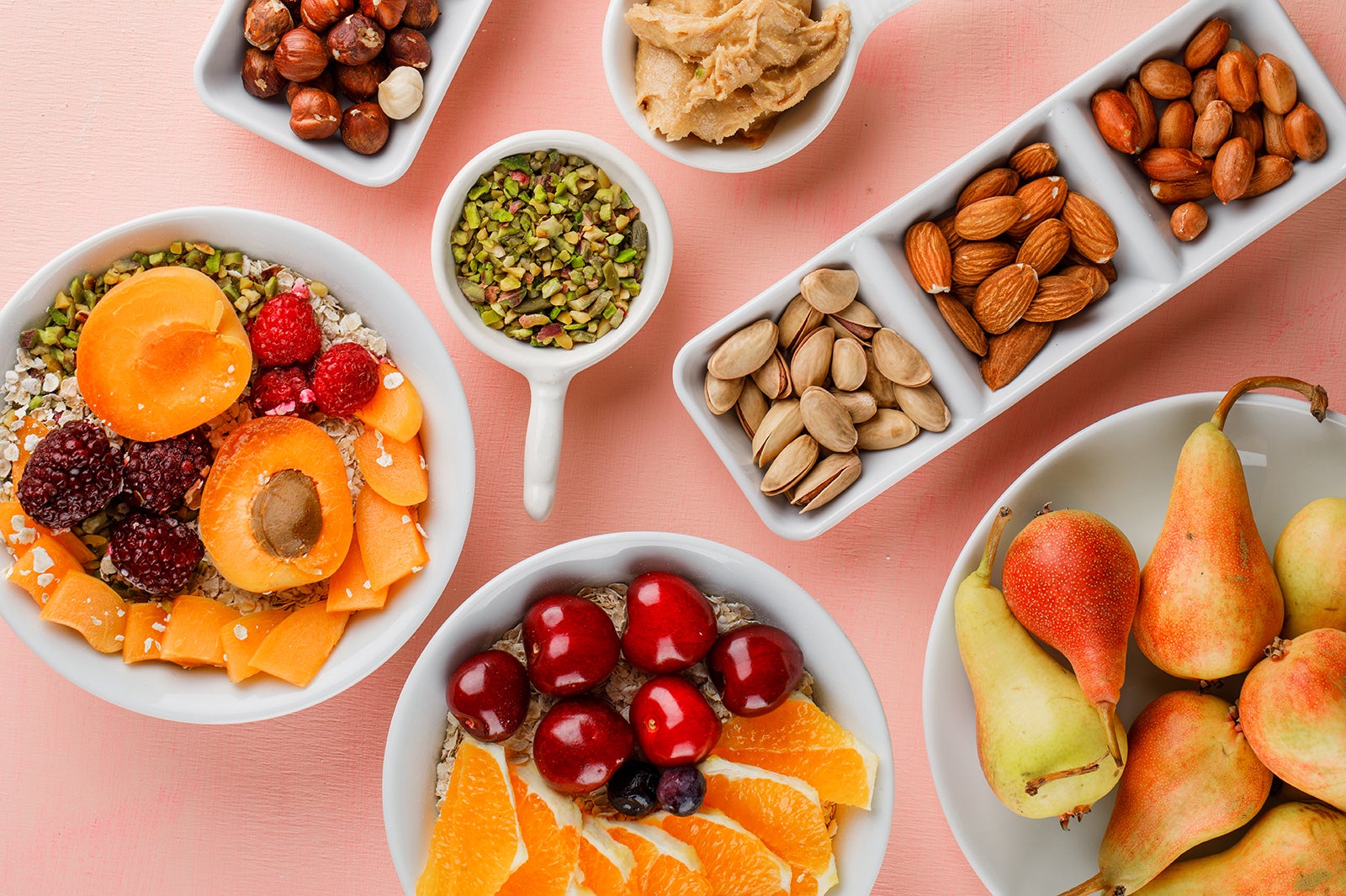 Overhead view of a table with bowls and plates of healthy food items, including fruits, oats and nuts.owls
