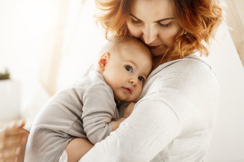 A red-headed woman holds a baby close to her chest.