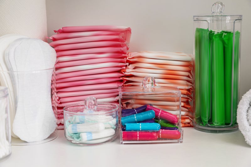 A cabinet shelf with a variety of products for menstrual cycles, including pads and tampons.
