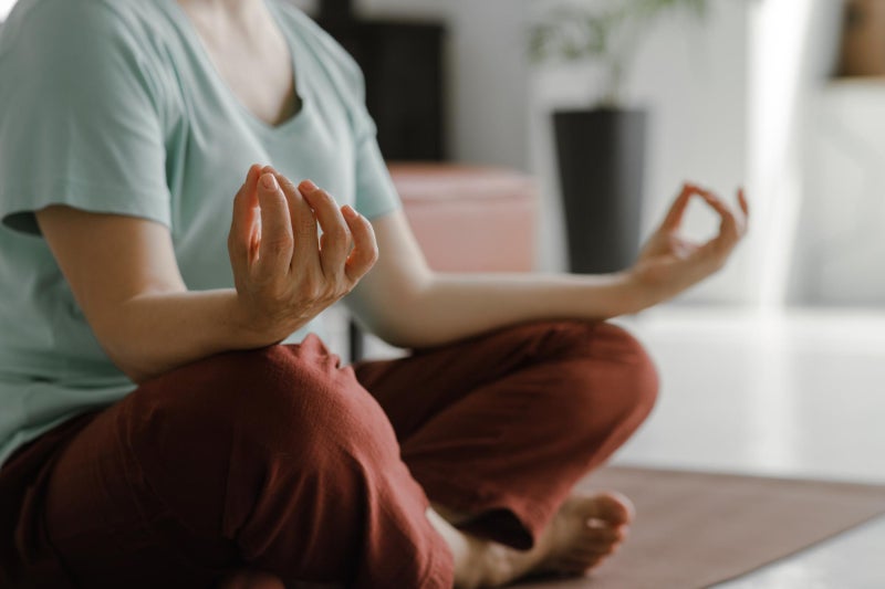 Unidentifiable woman sitting on the floor on a yoga mat crossing her legs and doing a meditation pose.