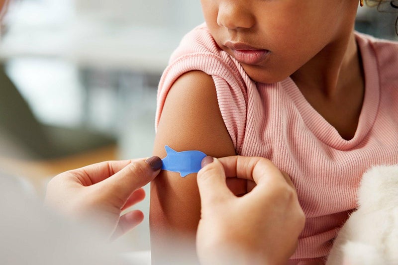 Young girl gets a band-aid on her right arm after an immunization shot.