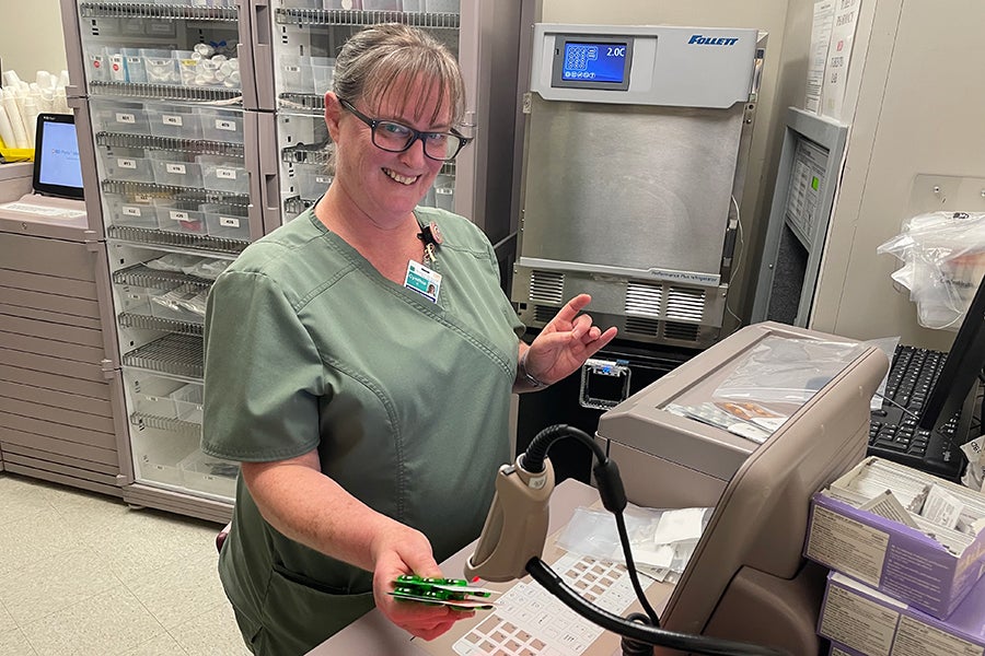 An employee in the laboratory holds a packet under a barcode scanner while smiling at the camera.