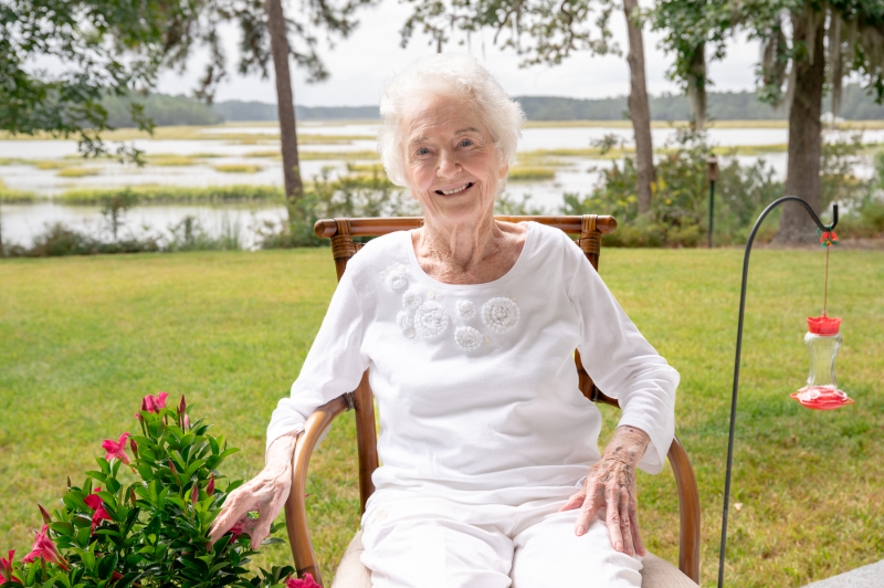 Mary McCarthy sits in a chair outside with a Lowcountry South Carolina marsh behind her in the background