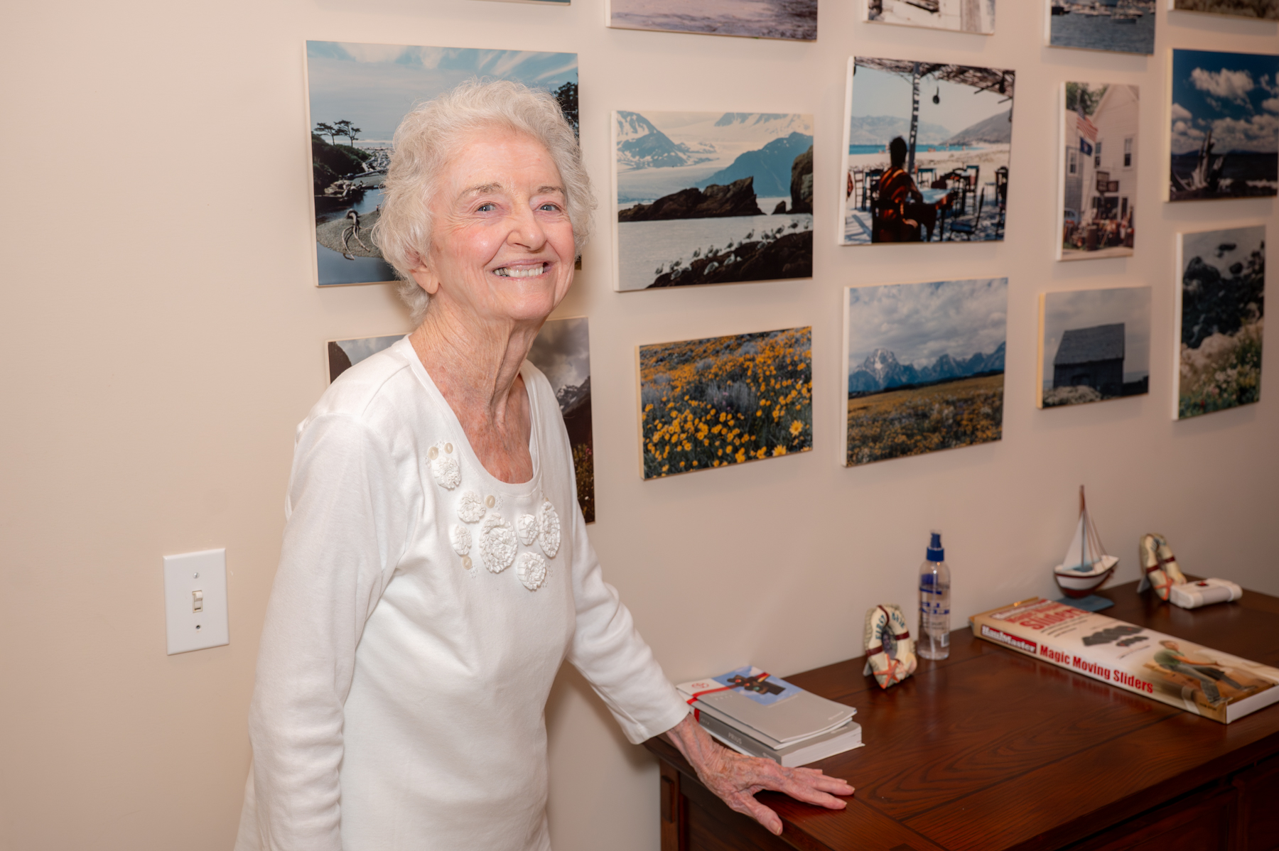 Mary McCarthy poses for a photo standing next to a side table with landscape photos on the wall behind her