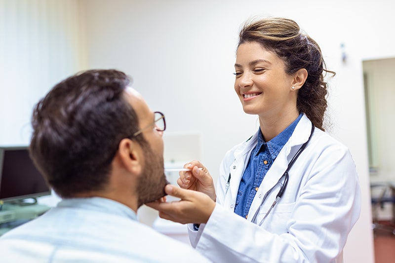 Female medical provider looking in the mouth of a male patient.