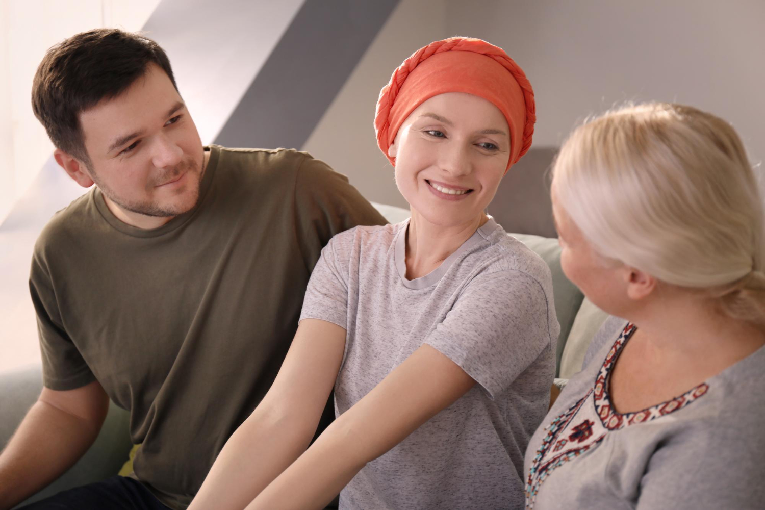 A young woman wearing a head covering sits between a man and a woman and smiles at the woman.
