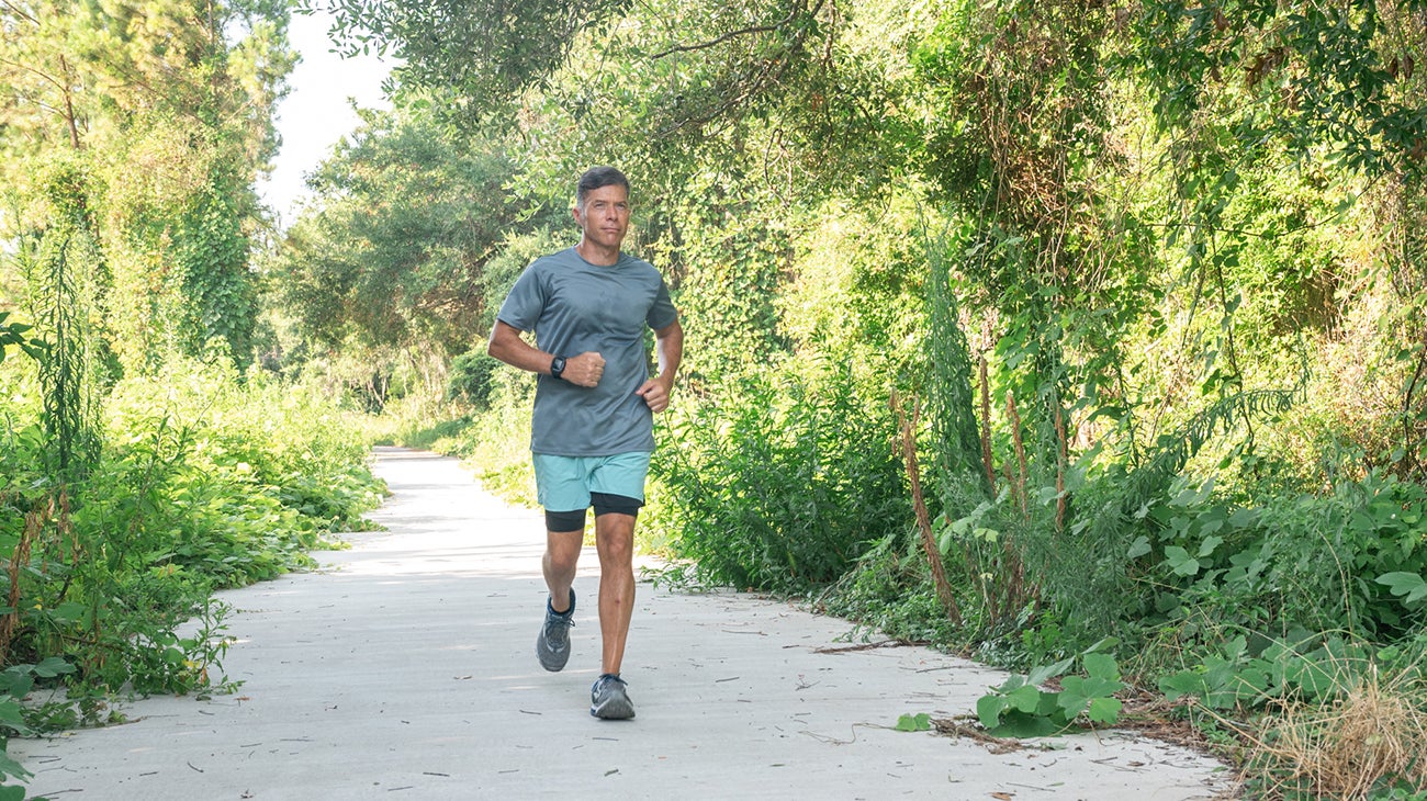 Man running down a paved, wooded running trail.