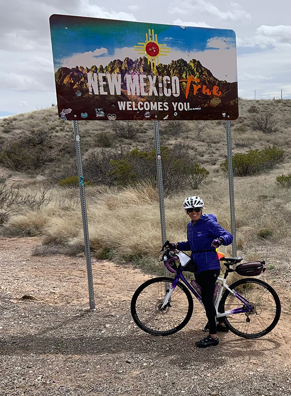 Cheryl Ruff in front of the New Mexico welcome sign on her bicycle