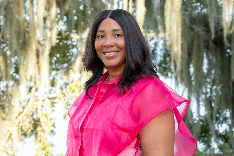 Victoria Carter, donned in a pink top, poses for a photo with Spanish moss draped oak trees in the background