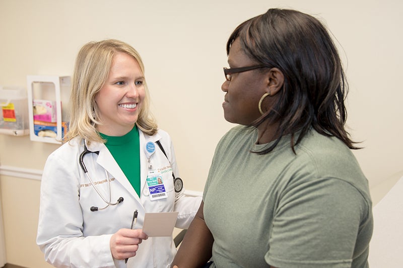 Mary Beth Donovan, NP smiles at a female patient in a clinical exam room.