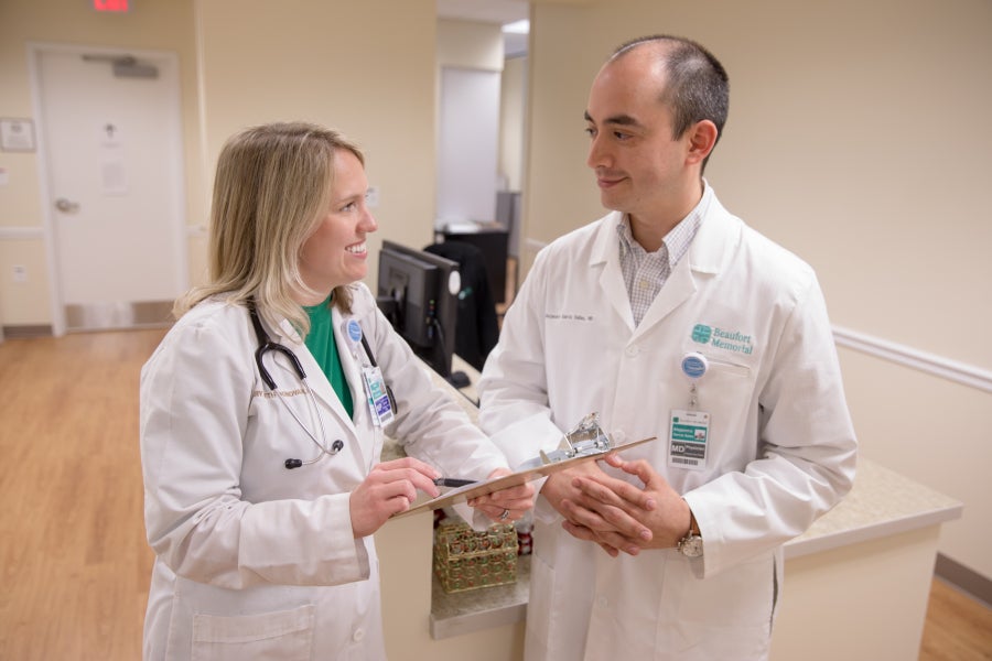 An advanced practice provider and a physician stand next to each other discussing a chart.