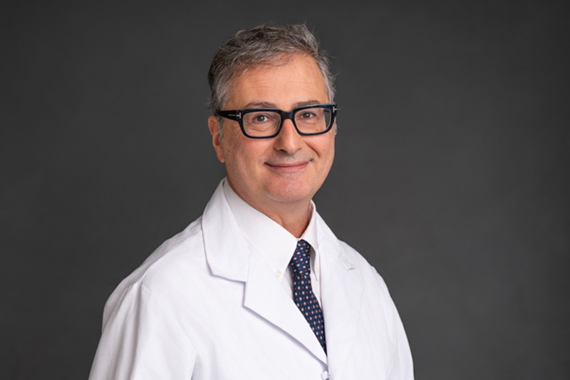 Professional headshot of Maurizio Buscarini, M.D., Ph.D., MPH-MBA in a white lab coat
