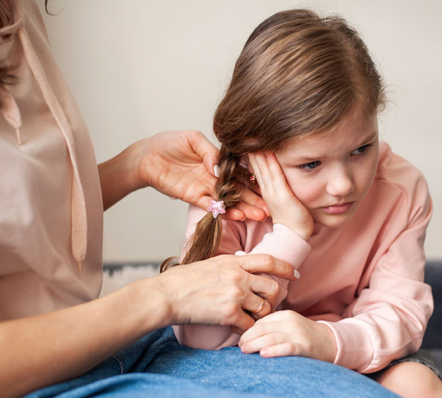 A little girl holding her ear with her hand and a guardian reaching for the child’s ear.