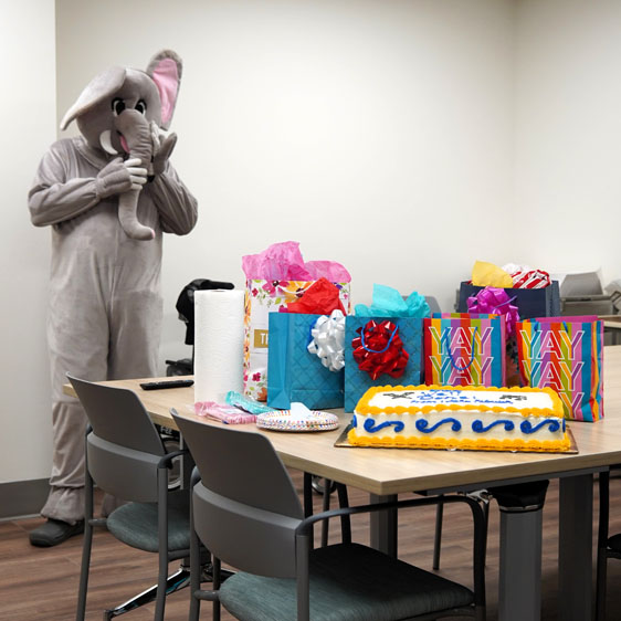 Banjo the mascot stands behind a table with gifts