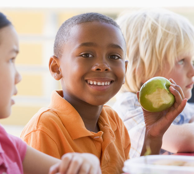 young boy enjoying an apple at lunch