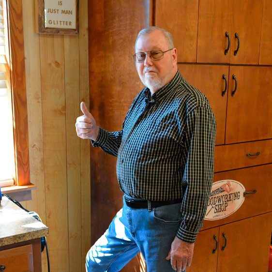 Larry Cook stands in his woodworking shop giving a thumbs up.