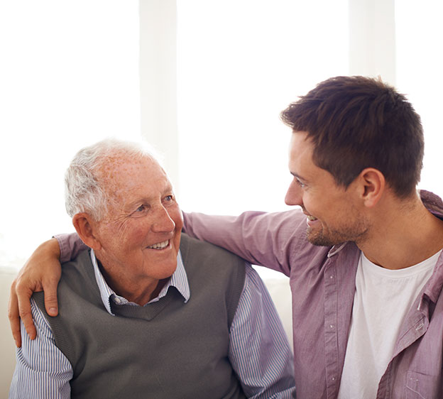 A young man sits on a couch with his arm around an older man.