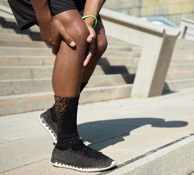 A person in activewear reaching for their knee as they descend an outdoor staircase
