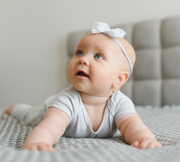 An infant crawling on the floor, looking upward and smiling