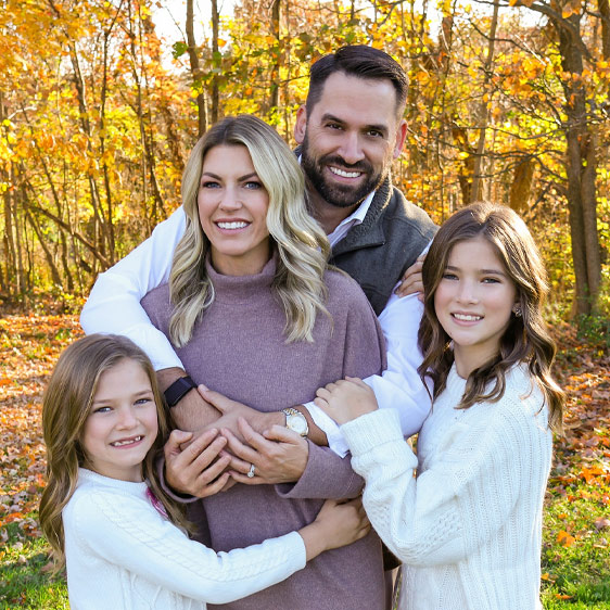 Breast surgeon Dr. Tara Grahovac with her husband and two daughters pose for a photo outdoors in the fall.